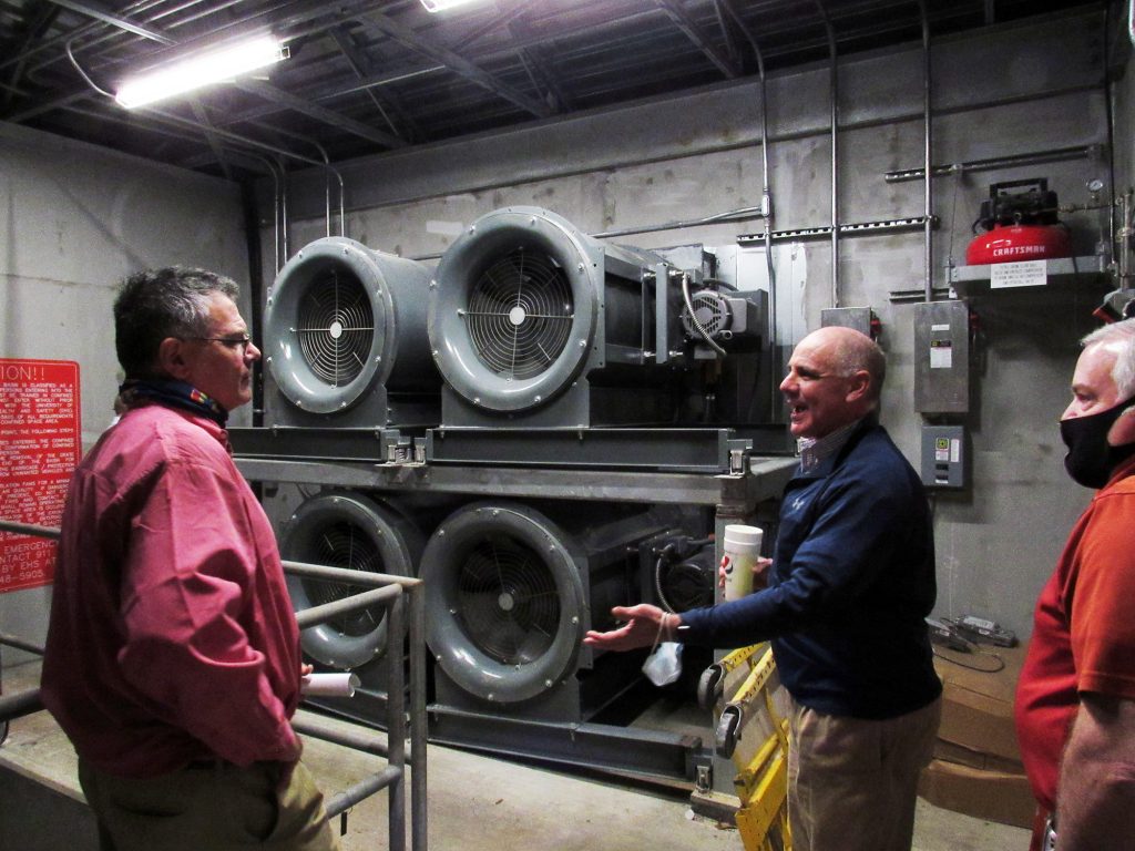 Three men in a concrete room with machinery.